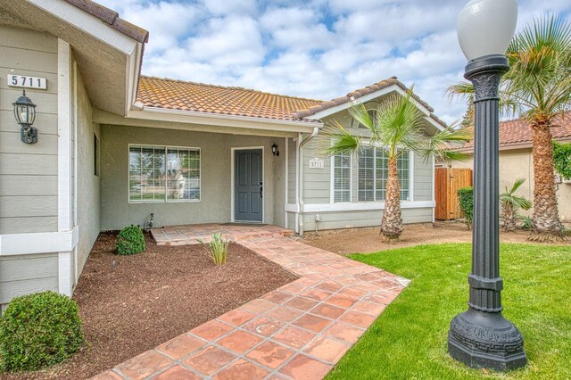 5711 W Fallon Ave, Fresno, CA 93722 - entrance to property featuring stucco siding, a yard, a tile roof, and fence