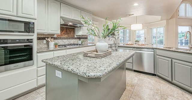 kitchen with a sink, decorative backsplash, under cabinet range hood, a kitchen island, and appliances with stainless steel finishes
