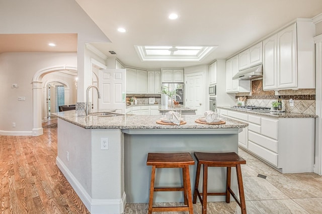kitchen with white cabinets, under cabinet range hood, arched walkways, decorative backsplash, and a breakfast bar area