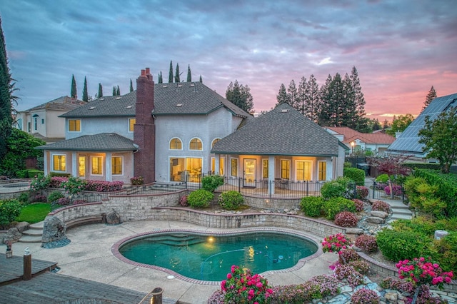 back of house at dusk with stucco siding, an outdoor pool, a chimney, and a patio