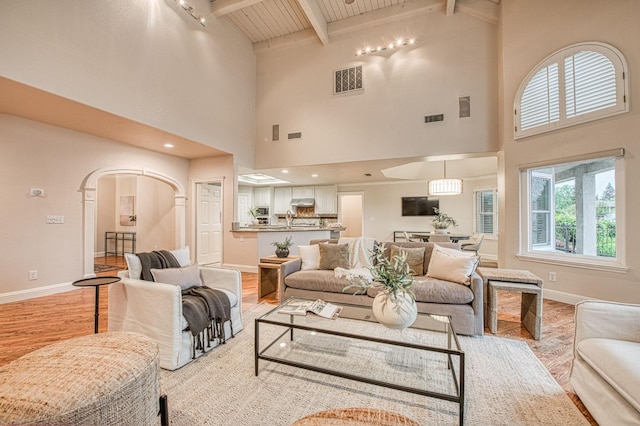 living room with light wood-type flooring, baseboards, visible vents, and high vaulted ceiling