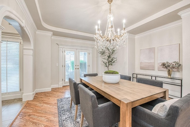dining area with crown molding, french doors, light wood-style flooring, a notable chandelier, and a raised ceiling