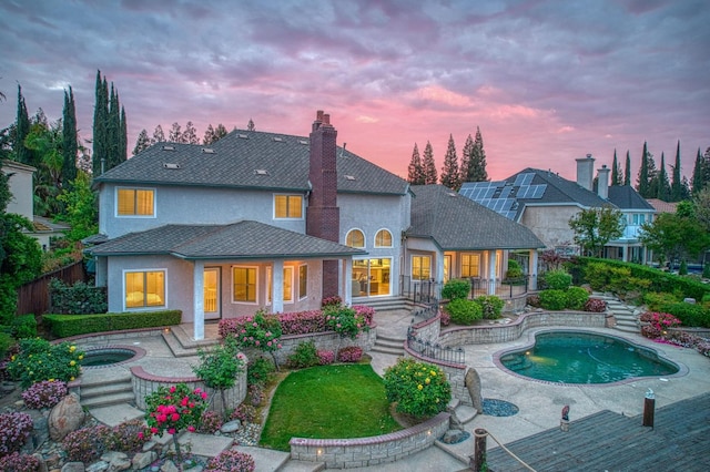 back of property at dusk featuring a fenced in pool, a chimney, covered porch, fence, and a jacuzzi
