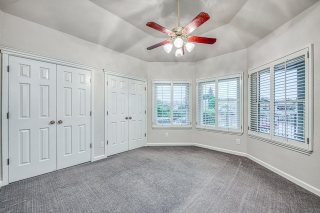 unfurnished bedroom featuring dark colored carpet, baseboards, two closets, and multiple windows