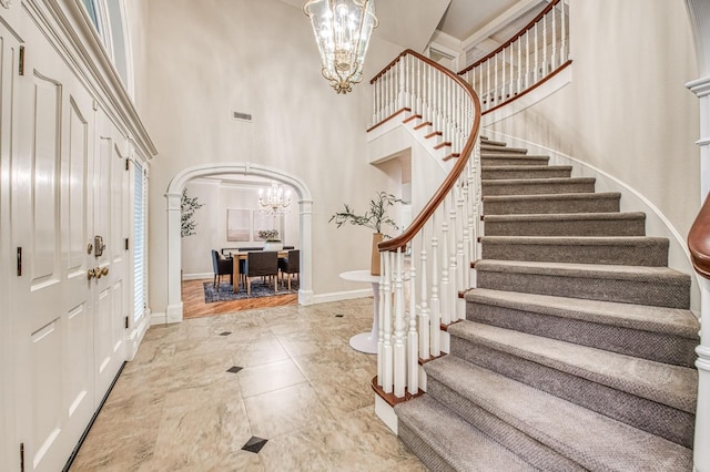entrance foyer with arched walkways, baseboards, a towering ceiling, an inviting chandelier, and stairs