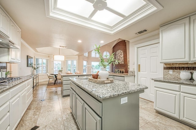 kitchen with stainless steel gas cooktop, a sink, visible vents, decorative backsplash, and a kitchen island
