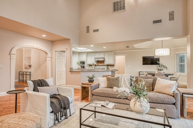 living area with light wood-style floors, visible vents, and a high ceiling