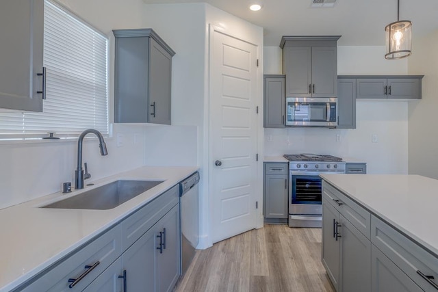 kitchen with light countertops, gray cabinetry, a sink, and appliances with stainless steel finishes