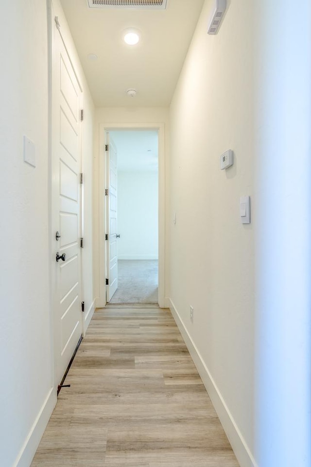 corridor featuring light wood finished floors, baseboards, and visible vents
