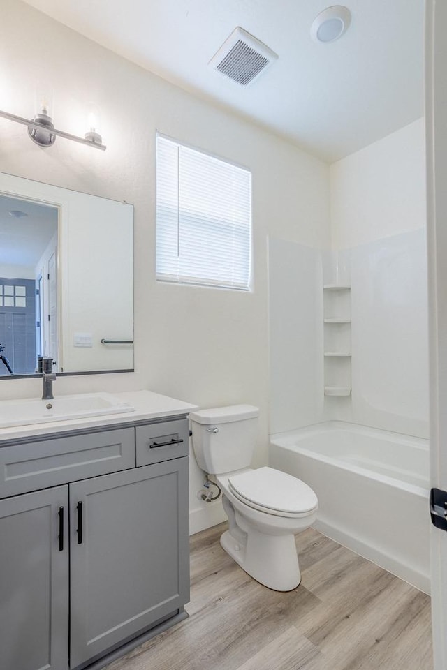 bathroom featuring wood finished floors, vanity,  shower combination, toilet, and visible vents