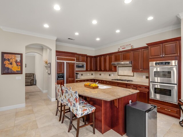 10640 N Old Course Dr, Fresno, CA 93730 - kitchen with under cabinet range hood, a sink, arched walkways, a kitchen island, and built in appliances
