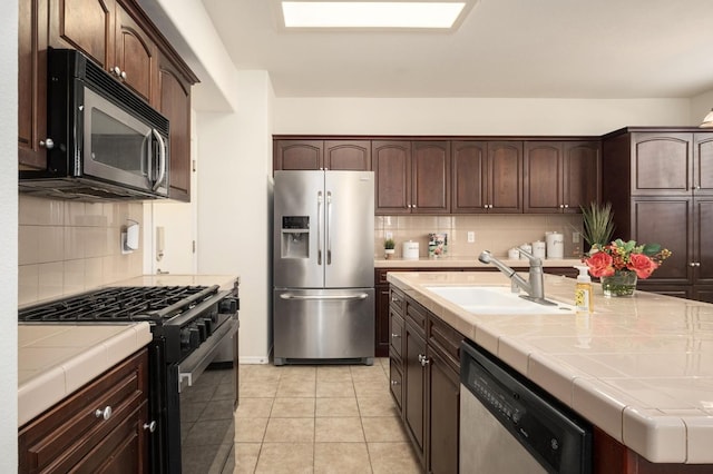 kitchen featuring stainless steel appliances, a sink, dark brown cabinets, decorative backsplash, and tile counters