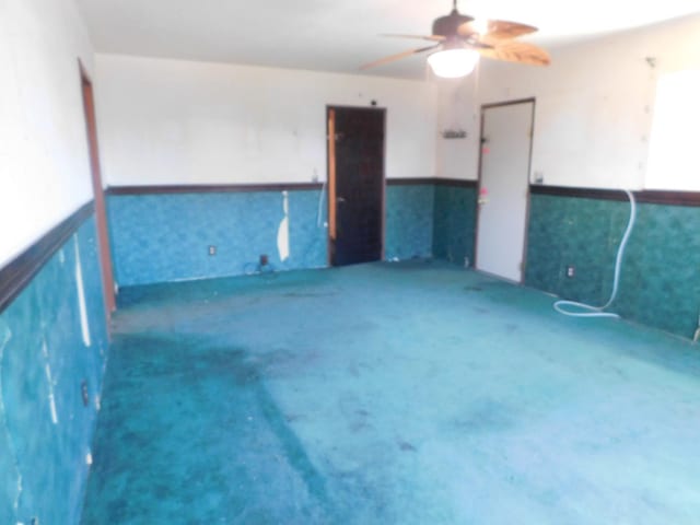 carpeted spare room with a ceiling fan and a wainscoted wall