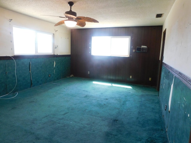 empty room with plenty of natural light, a ceiling fan, visible vents, and a textured ceiling