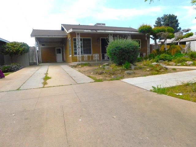 view of front of property with an attached carport, a porch, fence, concrete driveway, and stucco siding