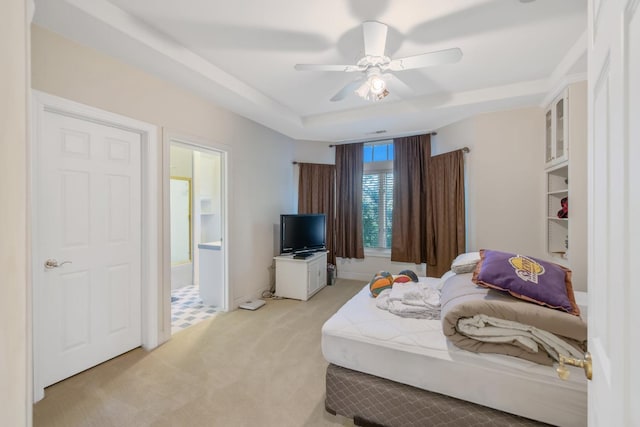bedroom featuring light carpet, a ceiling fan, ensuite bath, and a tray ceiling