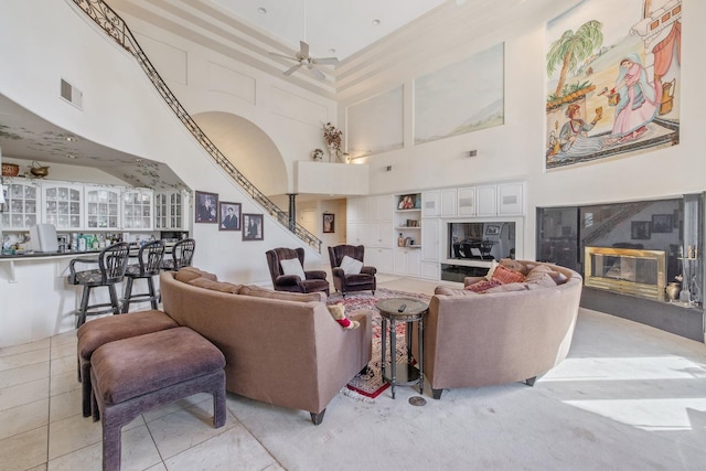 living area with a premium fireplace, a high ceiling, a ceiling fan, and visible vents
