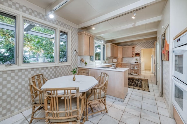 kitchen featuring a peninsula, light countertops, wallpapered walls, light brown cabinets, and rail lighting