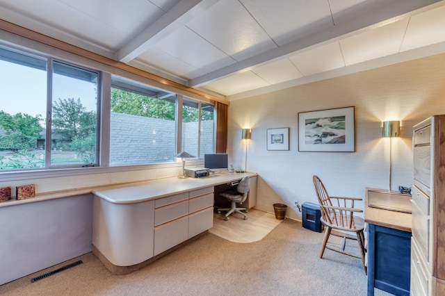 office area with built in desk, visible vents, beam ceiling, and light carpet