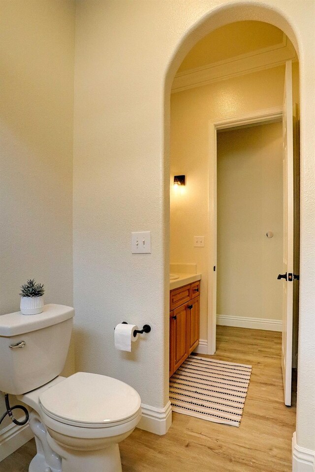 half bath featuring baseboards, toilet, ornamental molding, wood finished floors, and vanity