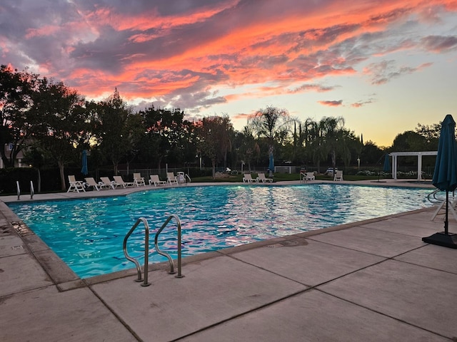 pool at dusk with fence, a patio, and a community pool