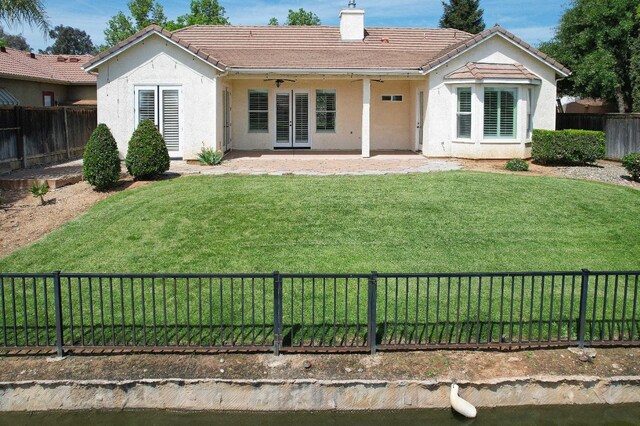 back of property with a chimney, a lawn, stucco siding, a ceiling fan, and a fenced backyard