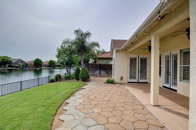 view of yard with ceiling fan, a water view, a patio, and a fenced backyard