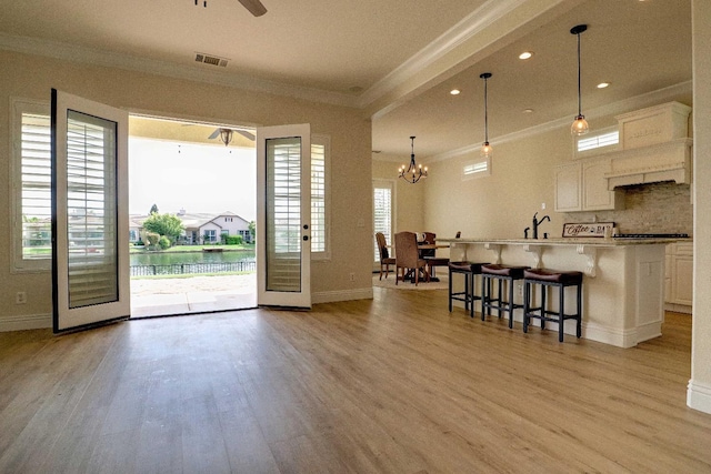 interior space featuring light wood-style flooring, visible vents, ornamental molding, and baseboards
