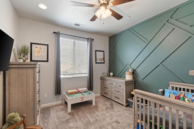 bedroom with a nursery area, light colored carpet, baseboards, and a ceiling fan