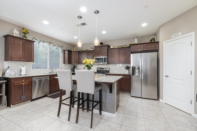 kitchen featuring stainless steel appliances, dark brown cabinets, decorative backsplash, and a kitchen bar