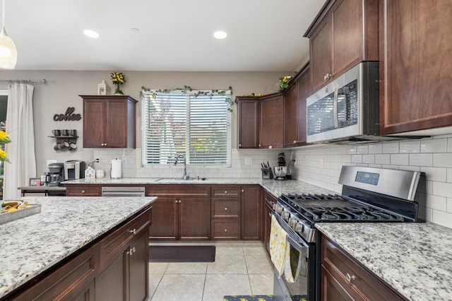 kitchen featuring decorative backsplash, light stone countertops, a sink, appliances with stainless steel finishes, and light tile patterned floors