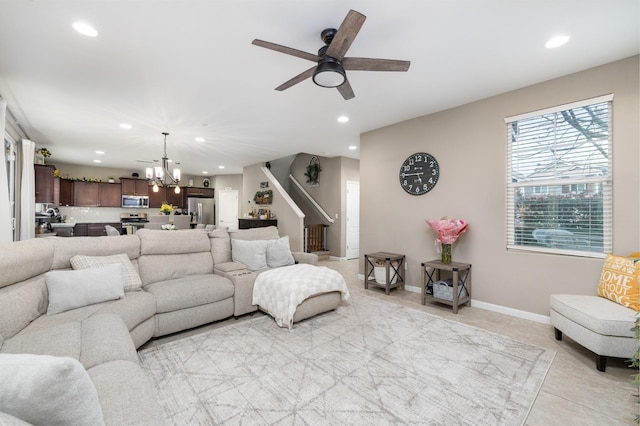 living area with light tile patterned flooring, ceiling fan with notable chandelier, recessed lighting, baseboards, and stairway