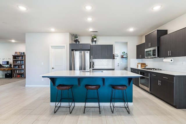 kitchen featuring a kitchen island with sink, appliances with stainless steel finishes, light countertops, a kitchen bar, and a sink