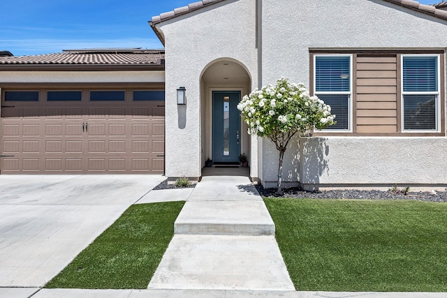 property entrance with concrete driveway, a tiled roof, an attached garage, a yard, and stucco siding
