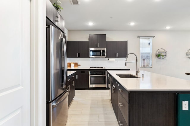 kitchen with tasteful backsplash, a sink, a kitchen island with sink, stainless steel appliances, and light countertops