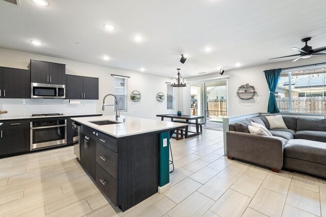 kitchen featuring dark cabinets, appliances with stainless steel finishes, open floor plan, and a sink