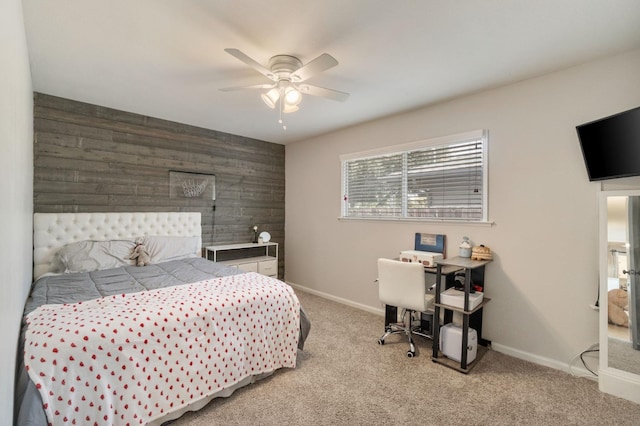 bedroom with wood walls, an accent wall, baseboards, light colored carpet, and ceiling fan