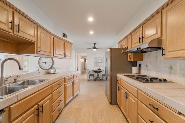 kitchen with stainless steel appliances, a sink, a ceiling fan, tile counters, and under cabinet range hood
