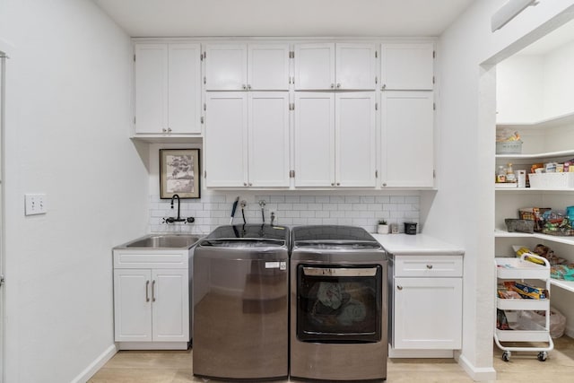clothes washing area with washing machine and dryer, baseboards, a sink, and cabinet space