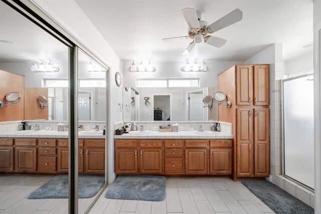 bathroom with ceiling fan, a sink, a shower stall, and double vanity
