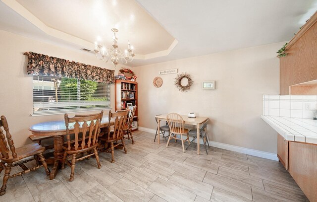 dining room with baseboards, an inviting chandelier, visible vents, and a raised ceiling
