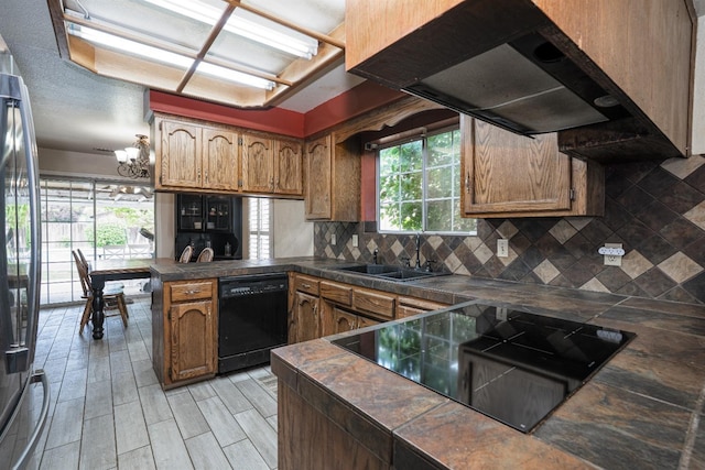 kitchen featuring tasteful backsplash, a sink, black appliances, a peninsula, and under cabinet range hood