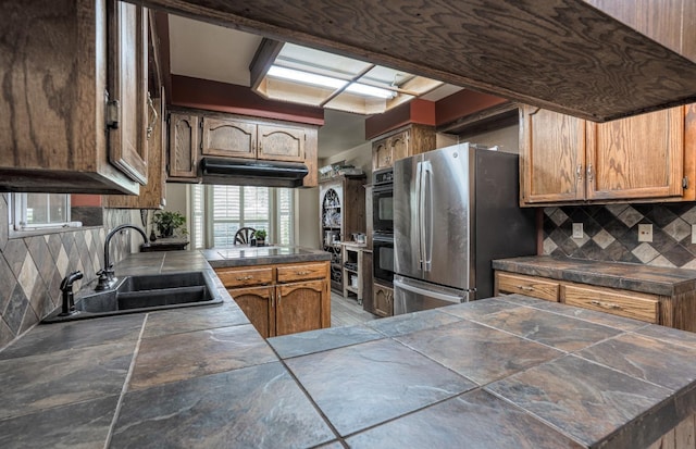 kitchen featuring a peninsula, freestanding refrigerator, decorative backsplash, and a sink