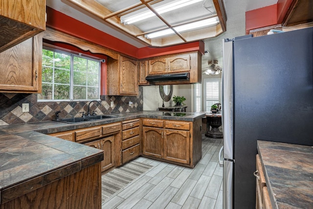 kitchen featuring brown cabinets, backsplash, a sink, freestanding refrigerator, and a peninsula