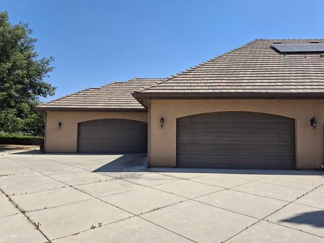 view of front of home with an attached garage, driveway, solar panels, and stucco siding