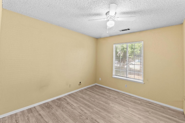 spare room with light wood finished floors, a textured ceiling, baseboards, visible vents, and a ceiling fan