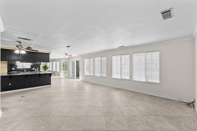 unfurnished living room with ornamental molding, a ceiling fan, visible vents, and light tile patterned floors