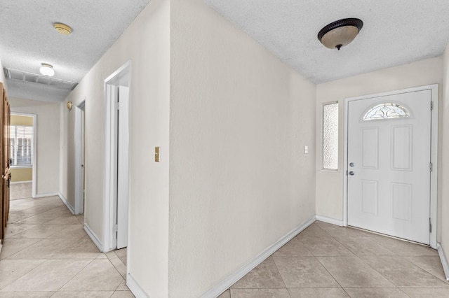 foyer entrance featuring baseboards, a textured ceiling, and light tile patterned floors