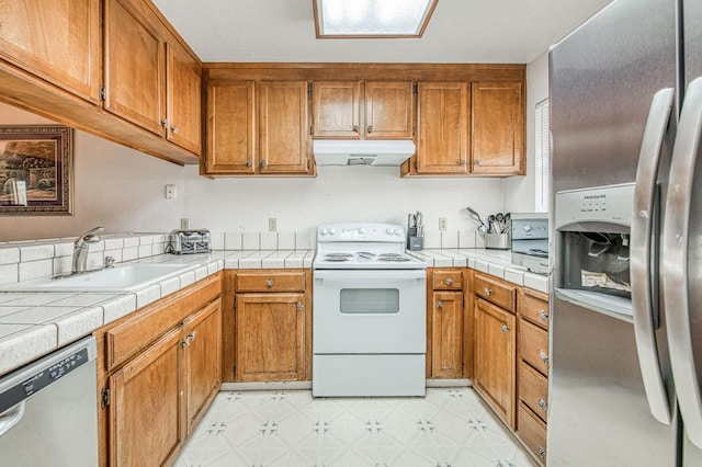 kitchen with stainless steel appliances, a sink, light floors, brown cabinetry, and under cabinet range hood