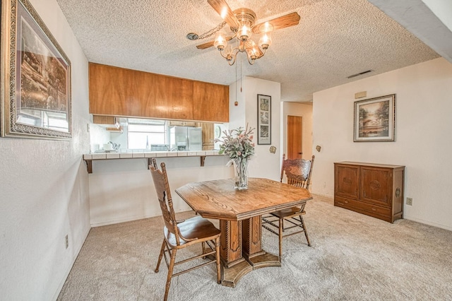 dining room featuring light carpet, a ceiling fan, visible vents, and a textured ceiling